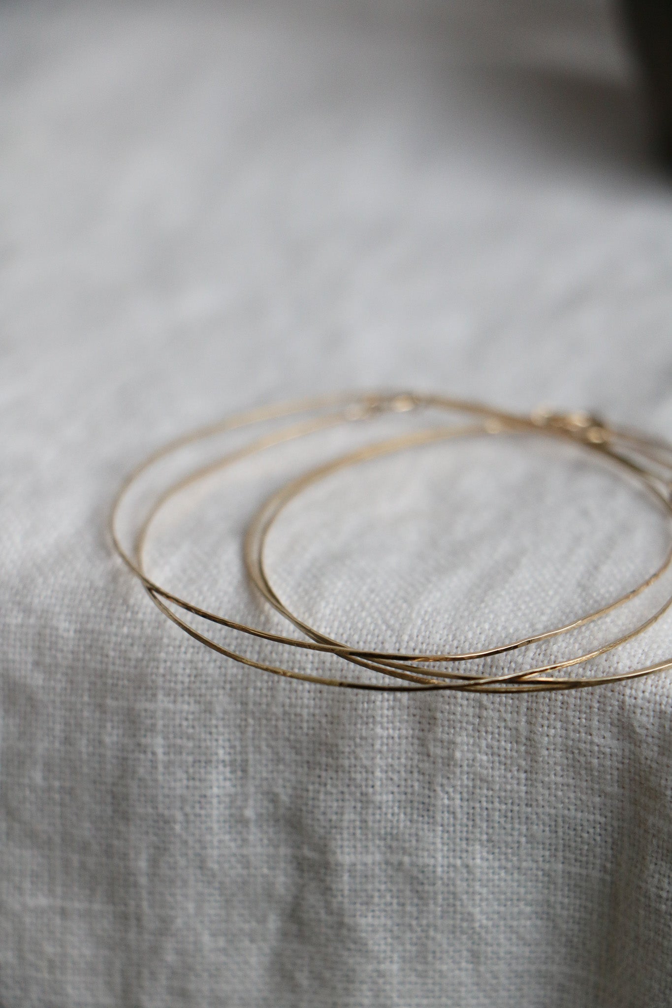 Flatlay of Charm City Links' handmade 14k gold bangles. Made individually in small batches, with 3-4 bangles sitting on a linen background.