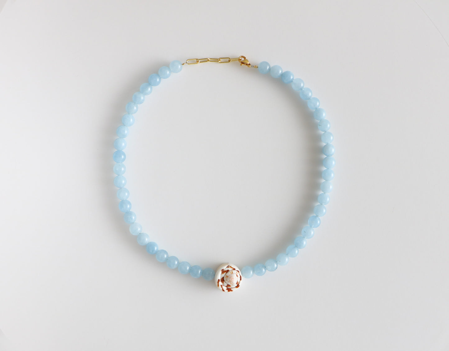 Beaded shell necklace, measuring 18'' in length with light blue beads around, a brown and white swirled shell at the bottom, and a gold clasp. Laying flat on a white background.