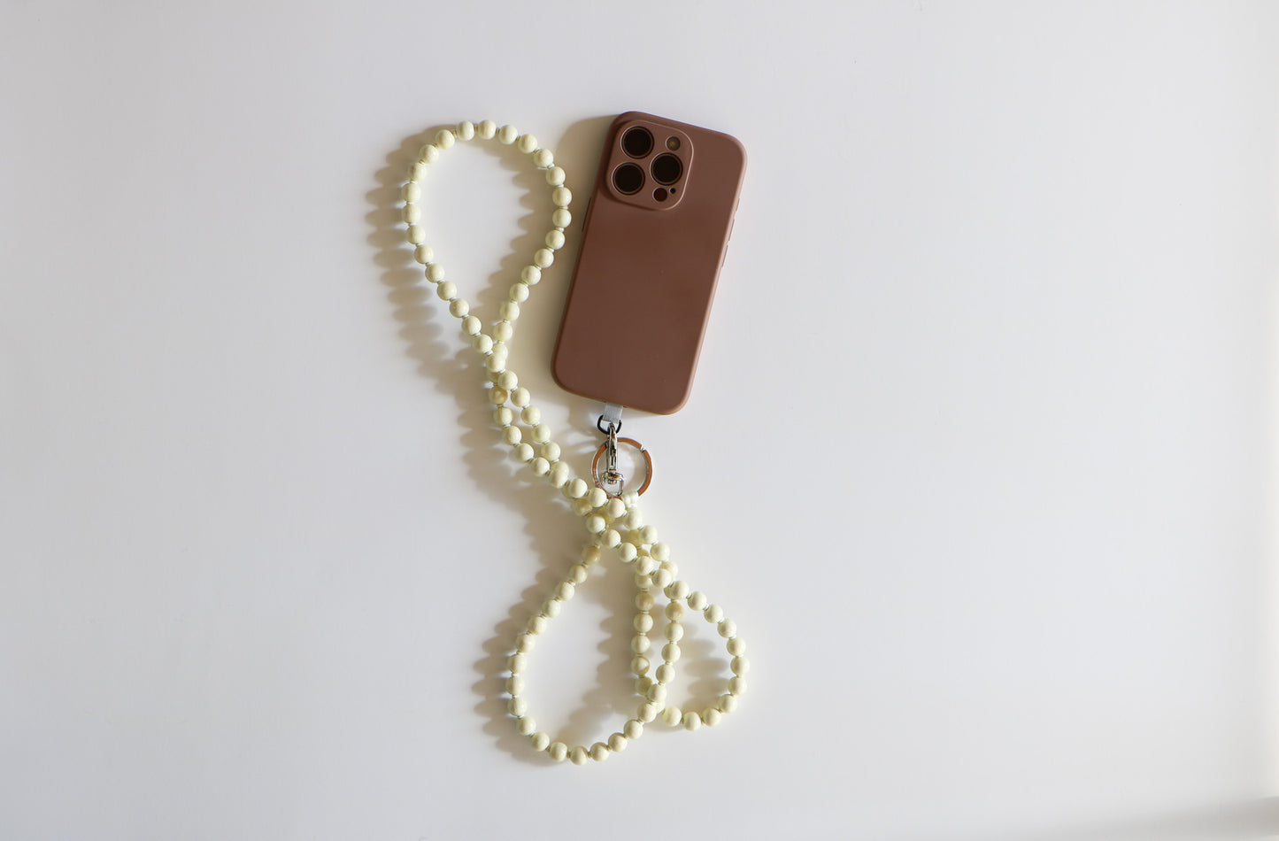 Phone with an opal white wooden beaded lanyard attached on a white flatlay background.