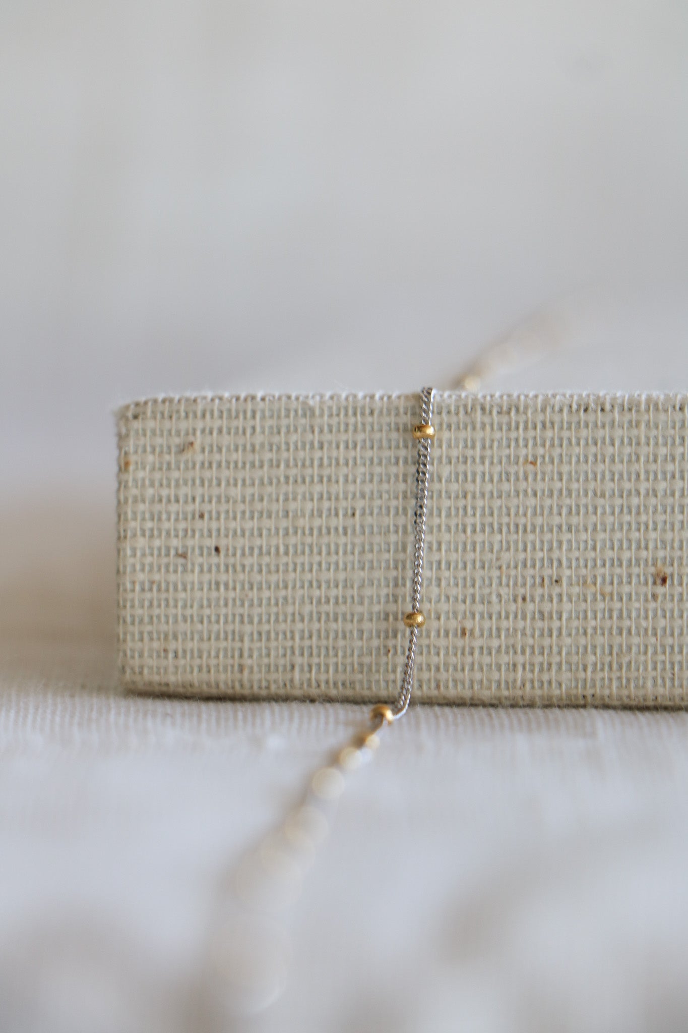 Permanent jewelry link, including white gold chain and yellow gold beads in between. Sitting on a woven background. 