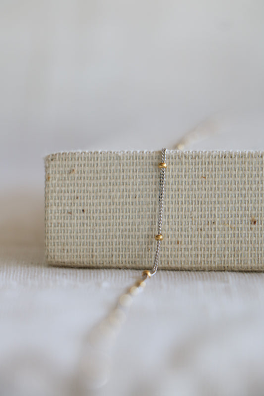 Permanent jewelry link, including white gold chain and yellow gold beads in between. Sitting on a woven background. 