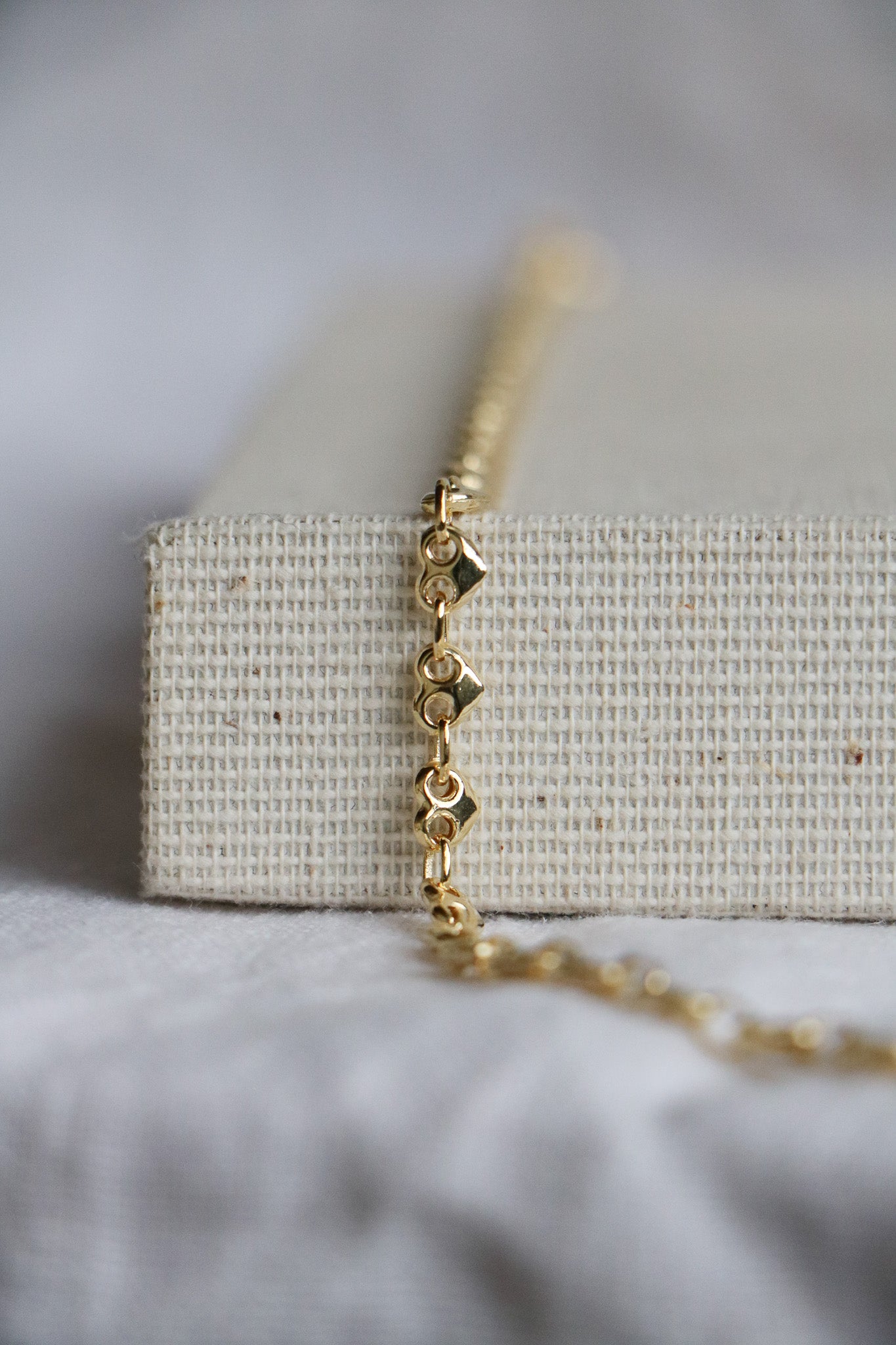 14k gold thick heart-shaped permanent jewelry link chain on a light woven background. Used as a permanent welded bracelet.