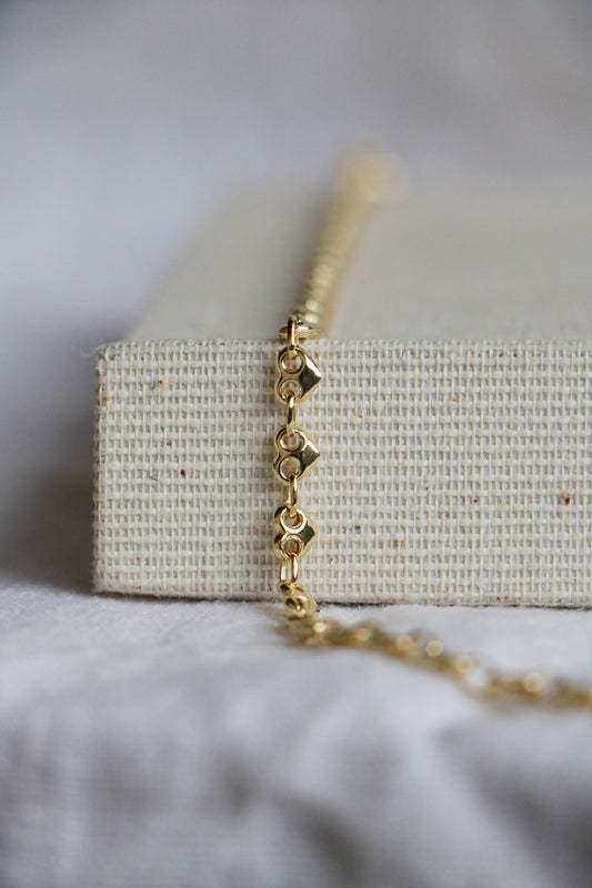 14k gold thick heart-shaped permanent jewelry link chain on a light woven background. Used as a permanent welded bracelet.