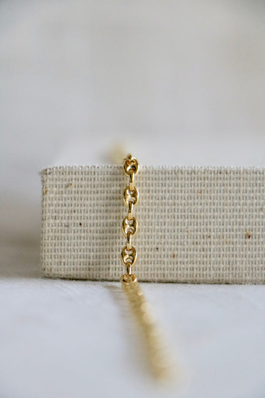 Statement permanent jewelry link, called the Gucci Link. Thick, 14k gold bracelet links on a woven jewelry holder and light blurred background.