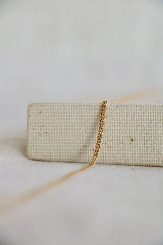 14k gold thick Curb Link by Charm City Links laying on a woven jewelry holder, representing a permanent jewelry bracelet or necklace. 