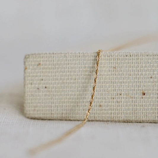 Twisted 14k gold chain used to make permanent jewelry including bracelets and necklaces at Charm City Links, on a woven jewelry holder.