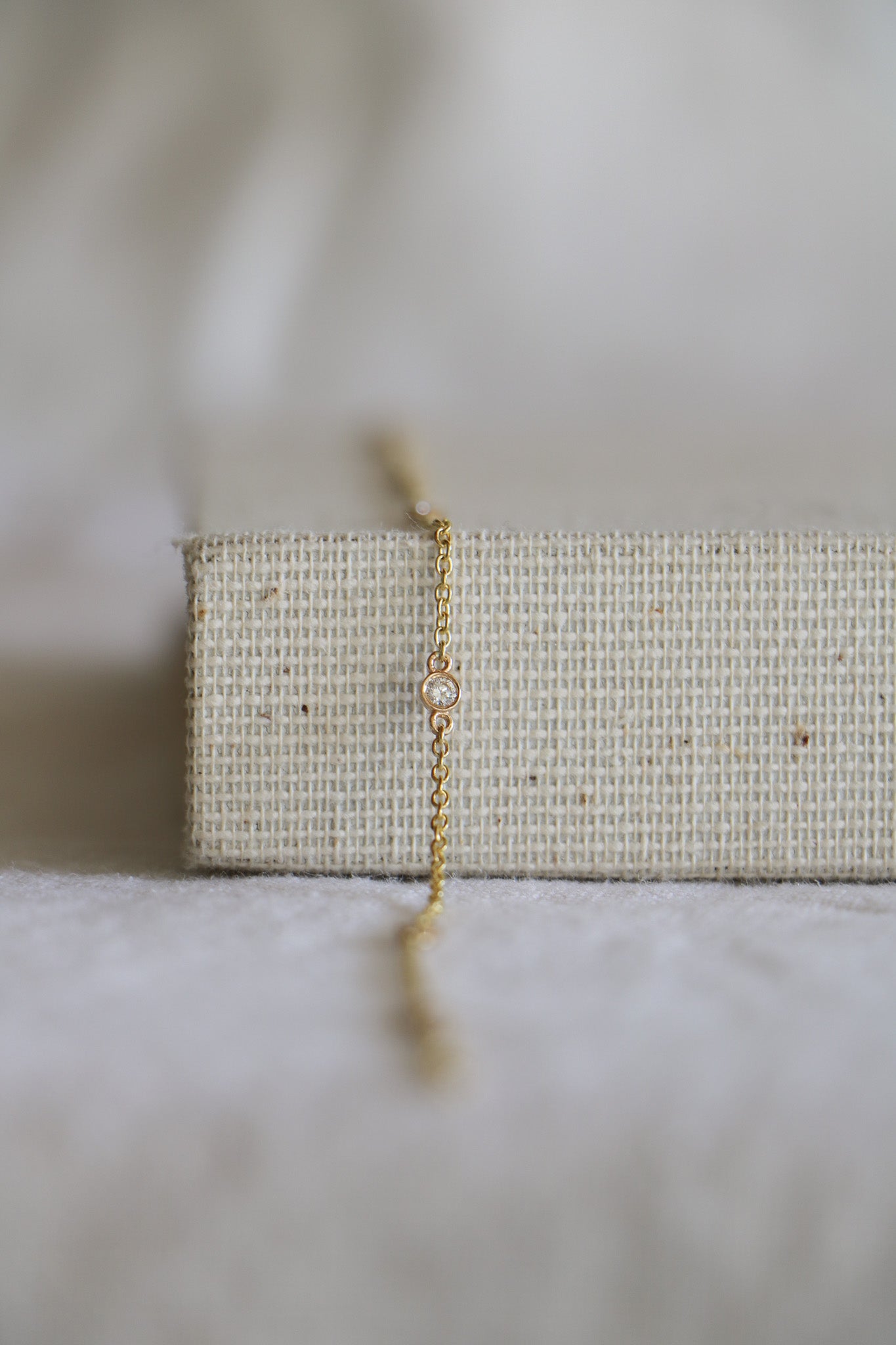 14k gold permanent jewelry chain, including gold chain links with a diamond connector at every inch. On a woven jewelry holder and blurred light background.