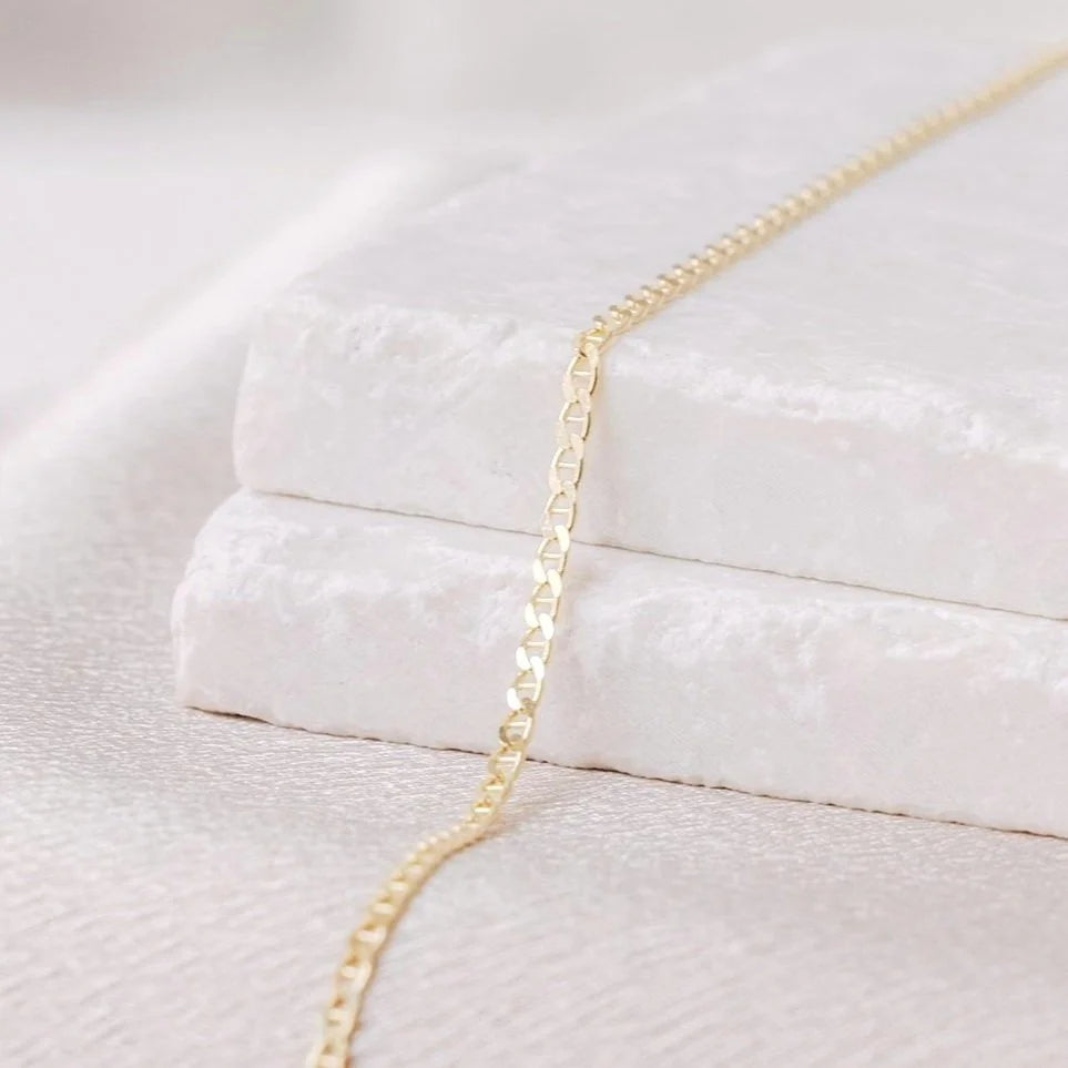 14k gold permanent jewelry link laying on a white stone background to represent permanent bracelet, necklace, or ring available at Charm City Links.