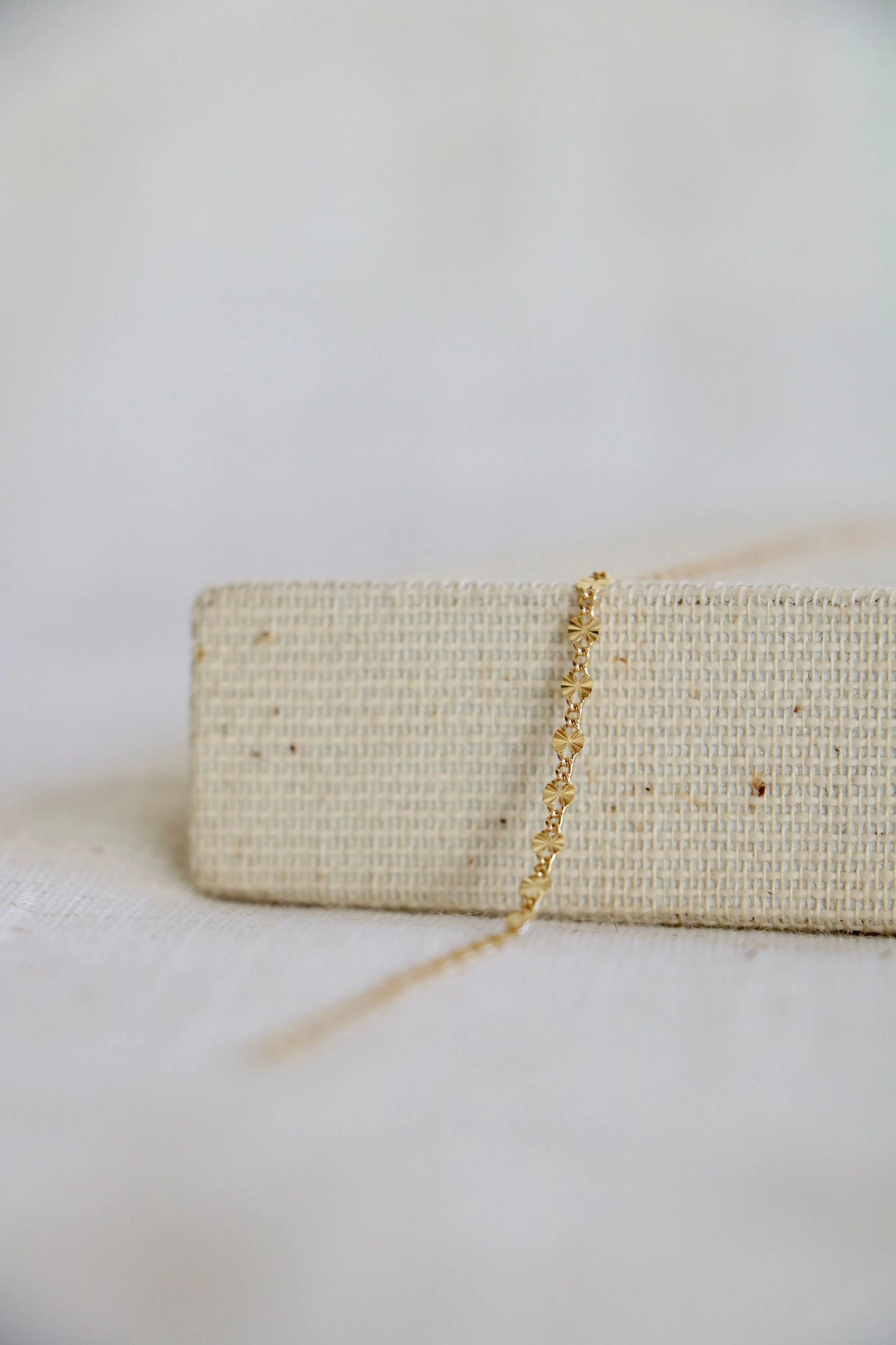 14k gold permanent jewelry chain with the link shapes of a starburst, laying on a woven jewelry holder with a muted linen background.