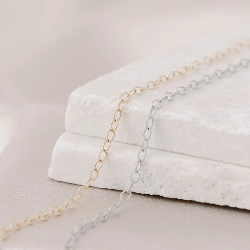 Two 14k gold jewelry chains laying side by side, one yellow gold, one white gold, and available to be made into permanent bracelets, anklets, or necklaces. Tarnish-resistant.