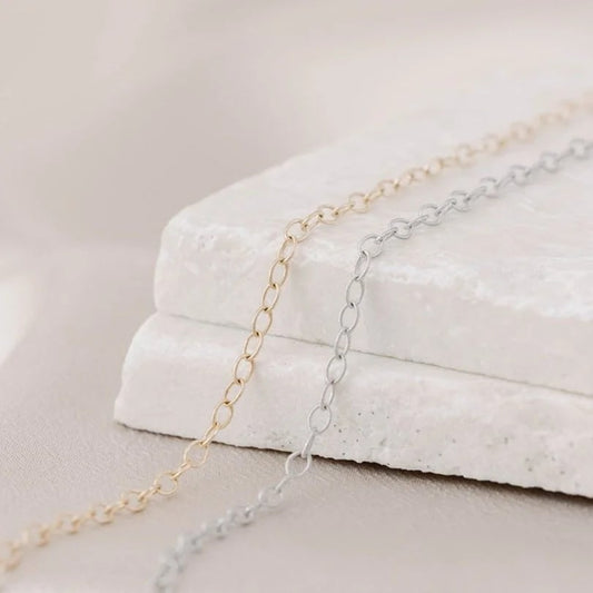 Two 14k gold jewelry chains laying side by side, one yellow gold, one white gold, and available to be made into permanent bracelets, anklets, or necklaces. Tarnish-resistant.