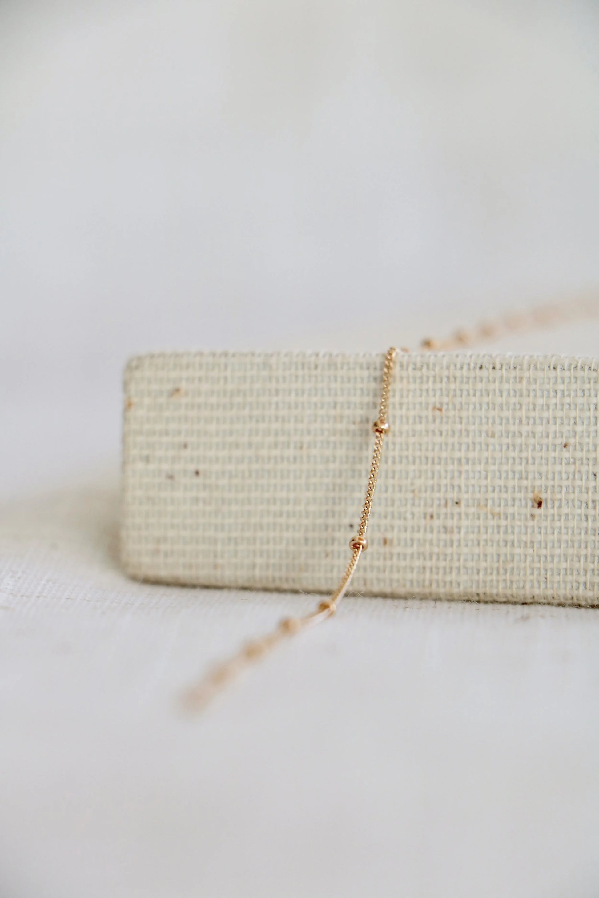 14k gold permanent jewelry chain on a woven holder with a light background. The link features a twisted chain with a small gold ball at every inch.