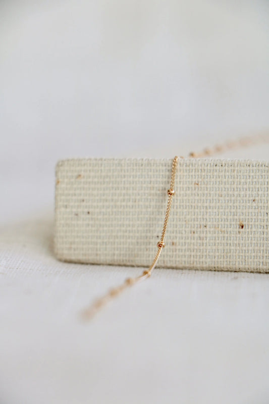 14k gold permanent jewelry chain on a woven holder with a light background. The link features a twisted chain with a small gold ball at every inch.