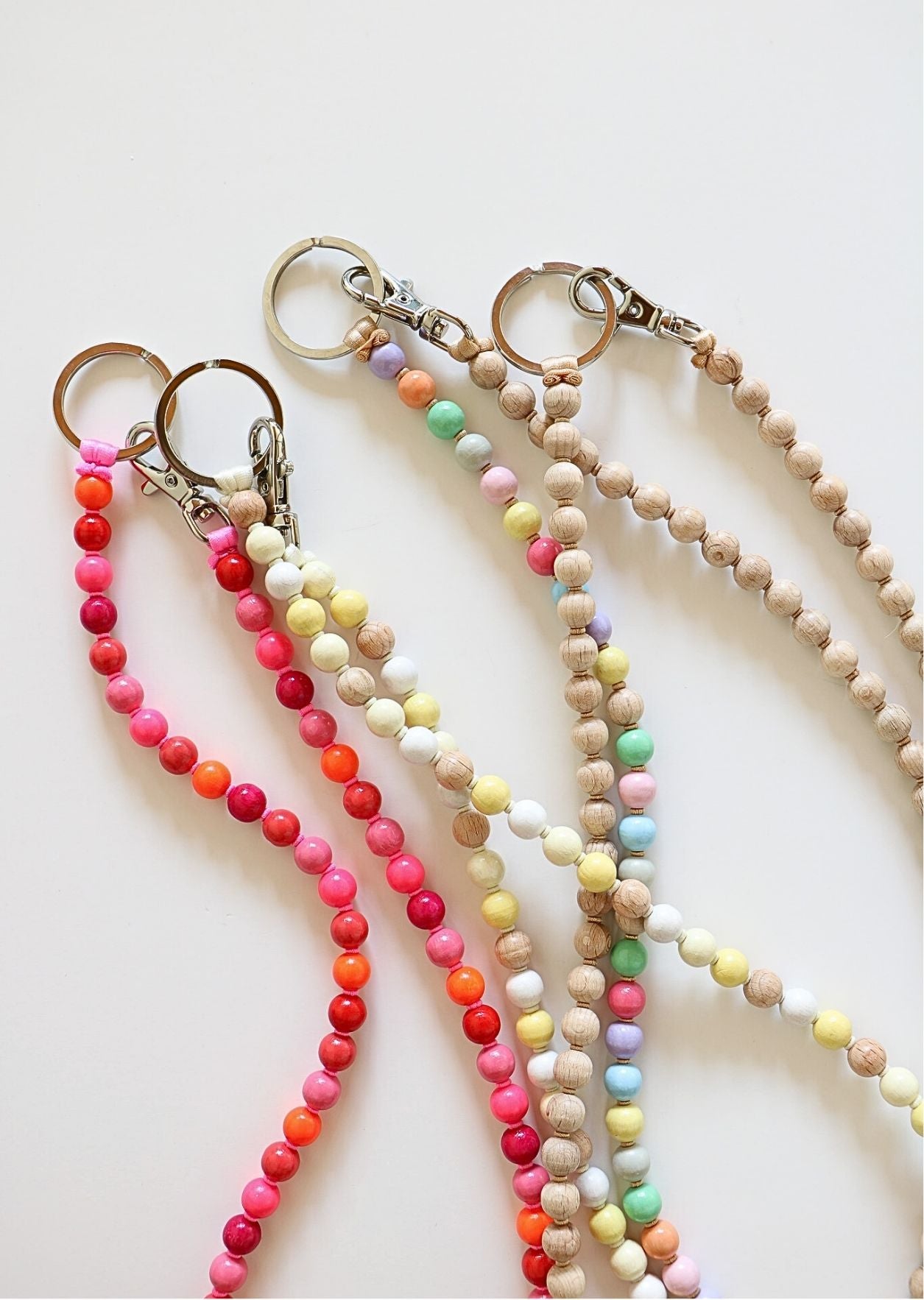 Multi-colored beaded keychains by Ina Seifart on a white background. Wooden beads in multicolored pink and red, pastel, and natural mix.