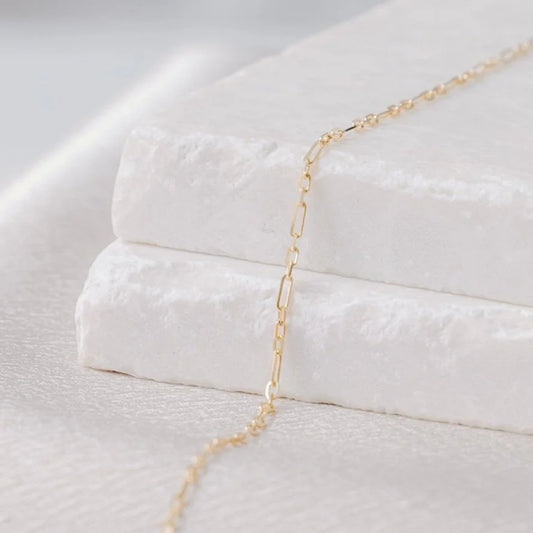 Bevelled oval permanent jewelry link in yellow gold on a light stone background, with the chain cascading down. 