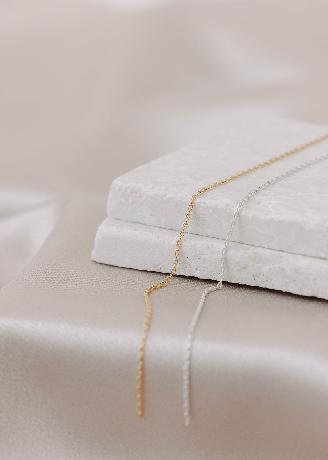 Two permanent bracelet chains side by side, one gold-filled, one-sterling silver, with links in a rectangle pattern on a light satin background. Showcasing Charm City Links' Dainty Rectangle Link.