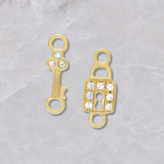 Two 14k yellow gold and diamond permanent jewelry connectors on a marble background. The left has a gold key with three diamonds on top, the right has a lock with 7 diamonds around the square lock. 