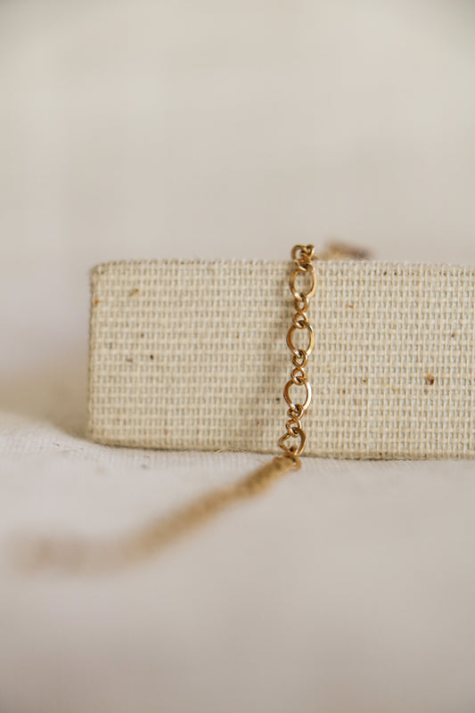 Gold-filled 'Figure 8 Link' on a woven jewelry holder with a light linen background. The link has gold oval links connected by smaller gold links that look like a figure 8. 