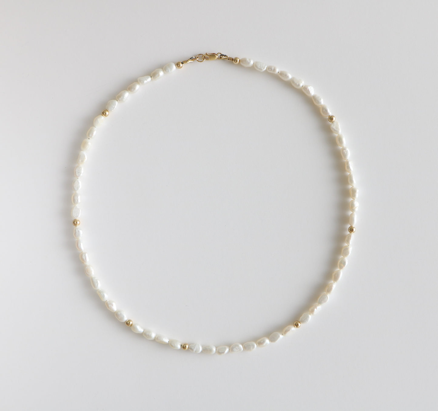 Necklace of freshwater pearls and gold filled beads interspersed throughout laying on a white background. The Freshwater Pearl necklace for Charm City Links.