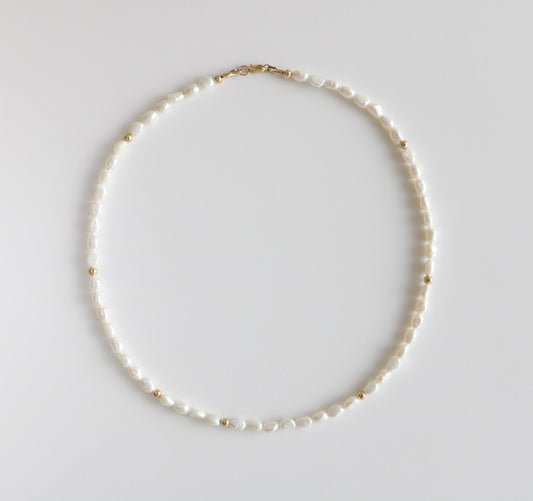 Necklace of freshwater pearls and gold filled beads interspersed throughout laying on a white background. The Freshwater Pearl necklace for Charm City Links.