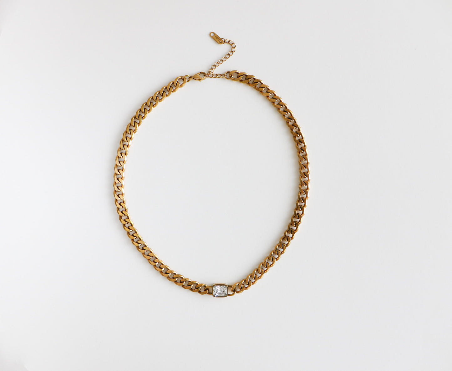 Chunky gold-filled chain necklace with a dainty diamond at the bottom, laying flat on a white background.