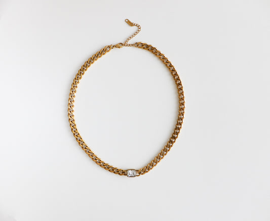 Chunky gold-filled chain necklace with a dainty diamond at the bottom, laying flat on a white background.