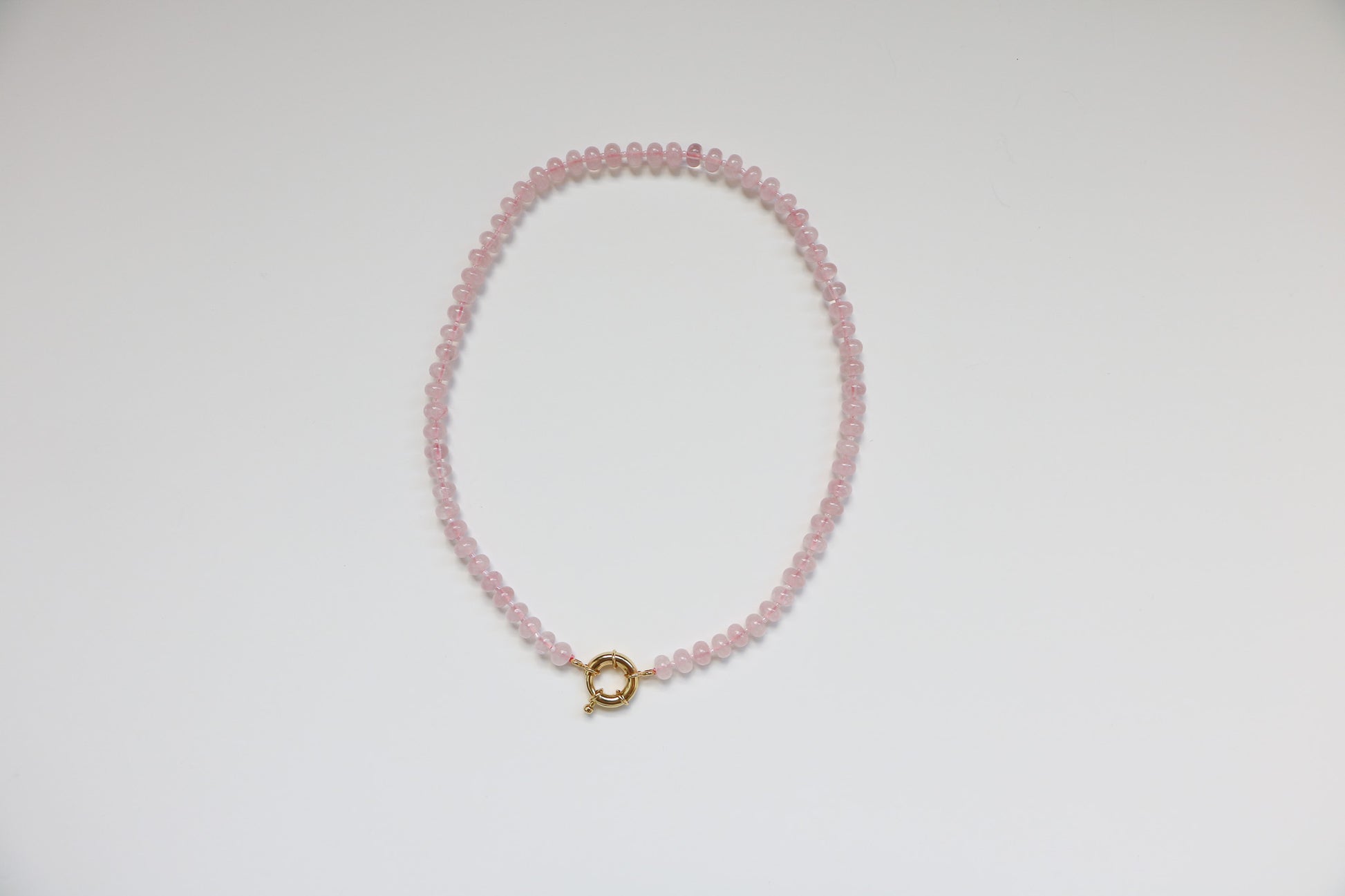 Natural gemstone beaded necklace in the color 'Bubblegum'. Light pink beads are connected in a 20'' necklace by a thick gold clasp, sitting on a white background. 