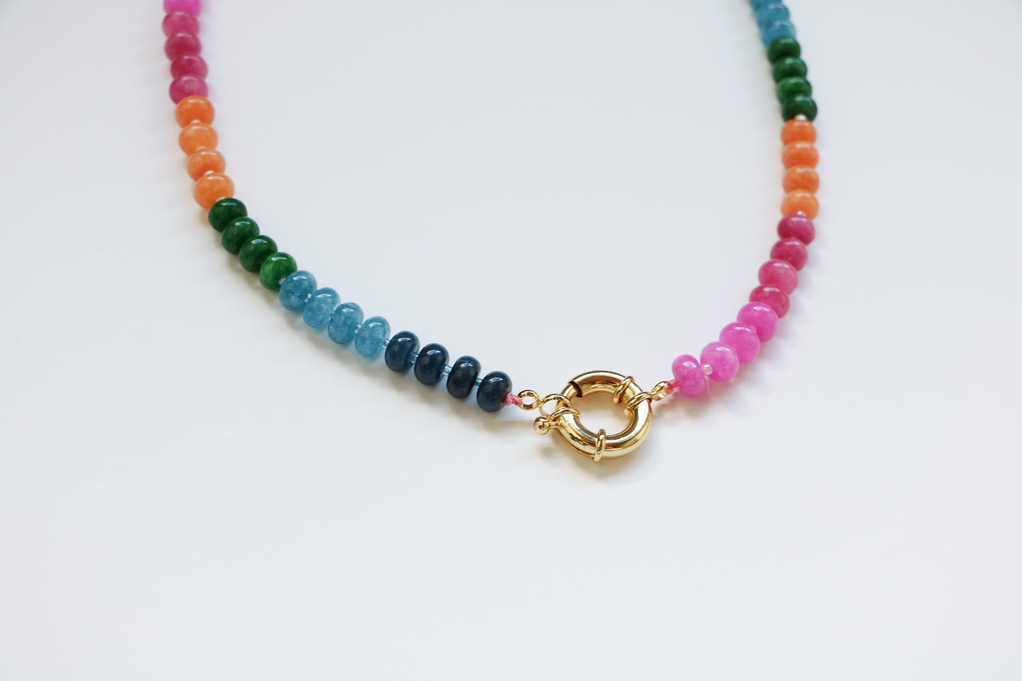 Close-up of the Harper Necklace in 'Candy' which focuses on the thick gold circular clasp. You can see the natural gemstone beads by the clasp in pink, blue, green, and orange. 