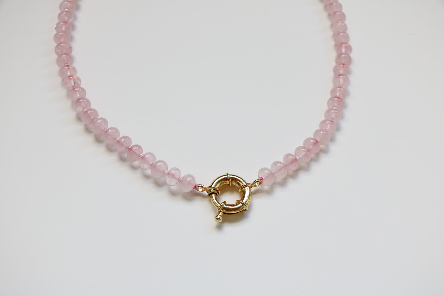 Close-up of the Harper Bubblegum Necklace from Charm City Links, showing the light pink gemstone beads in a circle on a flatlay, with details focusing on the thick gold clasp. 