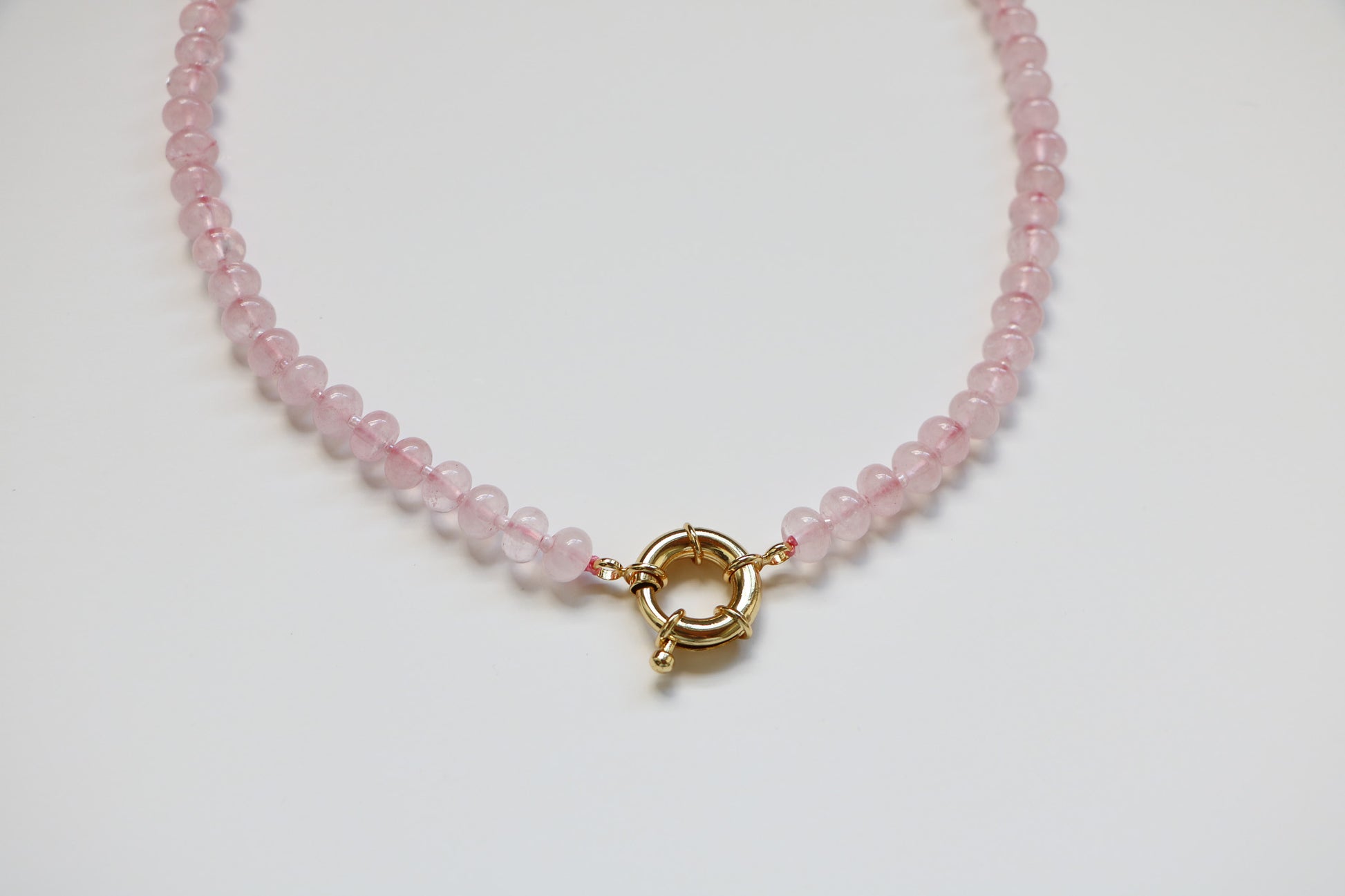 Close-up of the Harper Bubblegum Necklace from Charm City Links, showing the light pink gemstone beads in a circle on a flatlay, with details focusing on the thick gold clasp. 