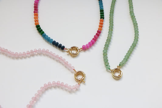 Three natural gemstone beaded necklaces  laying on a white background. All are connected by a thick gold clasp. The left is a bubblegum color, the middle is their 'candy necklace' option of rainbow beads, and the right is a seafoam green color. 