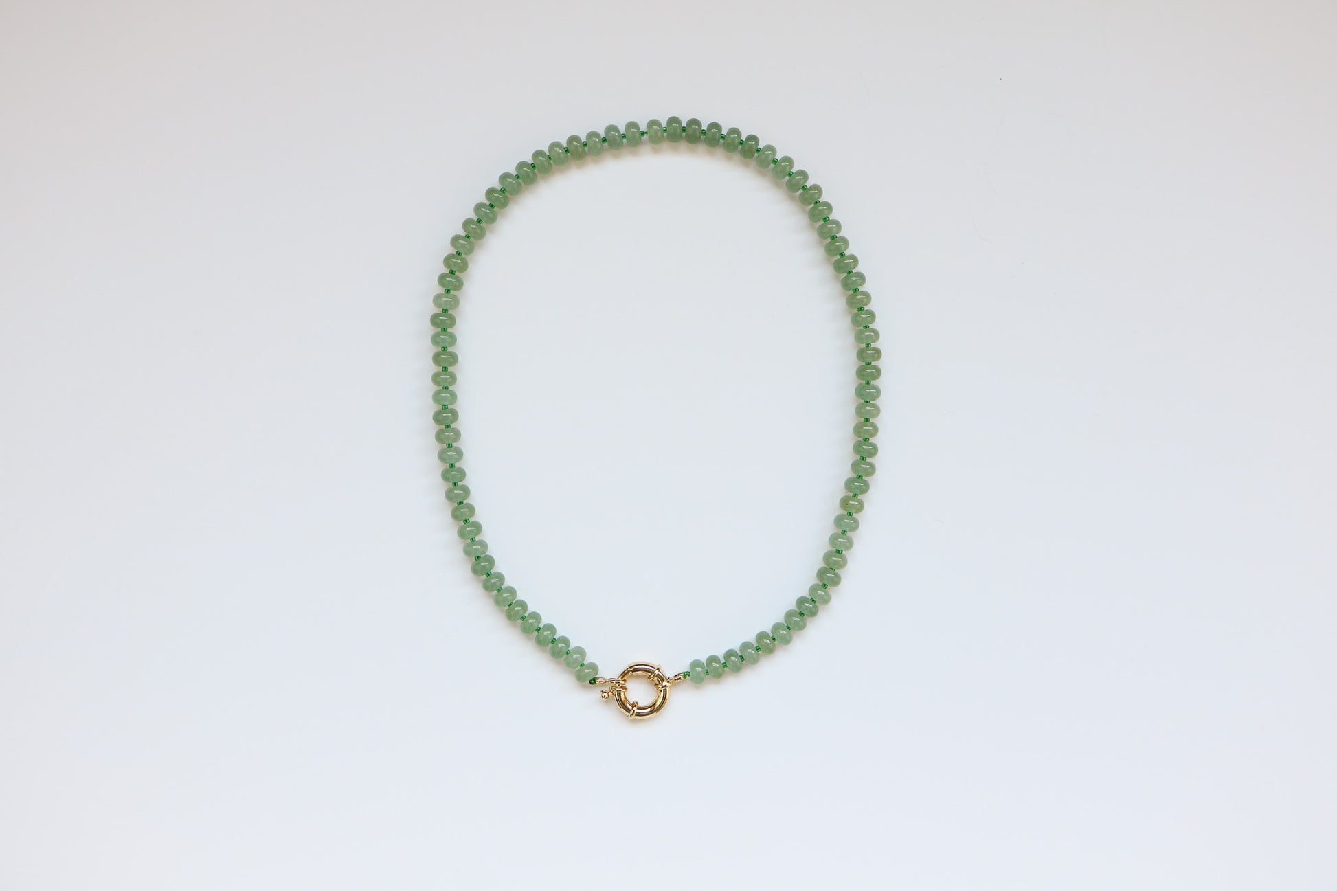 Flatlay of the Harper Necklace in Seafoam by Charm City Links. Shows the 20'' necklace with light green gemstone beads connected by a thick gold clasp. 