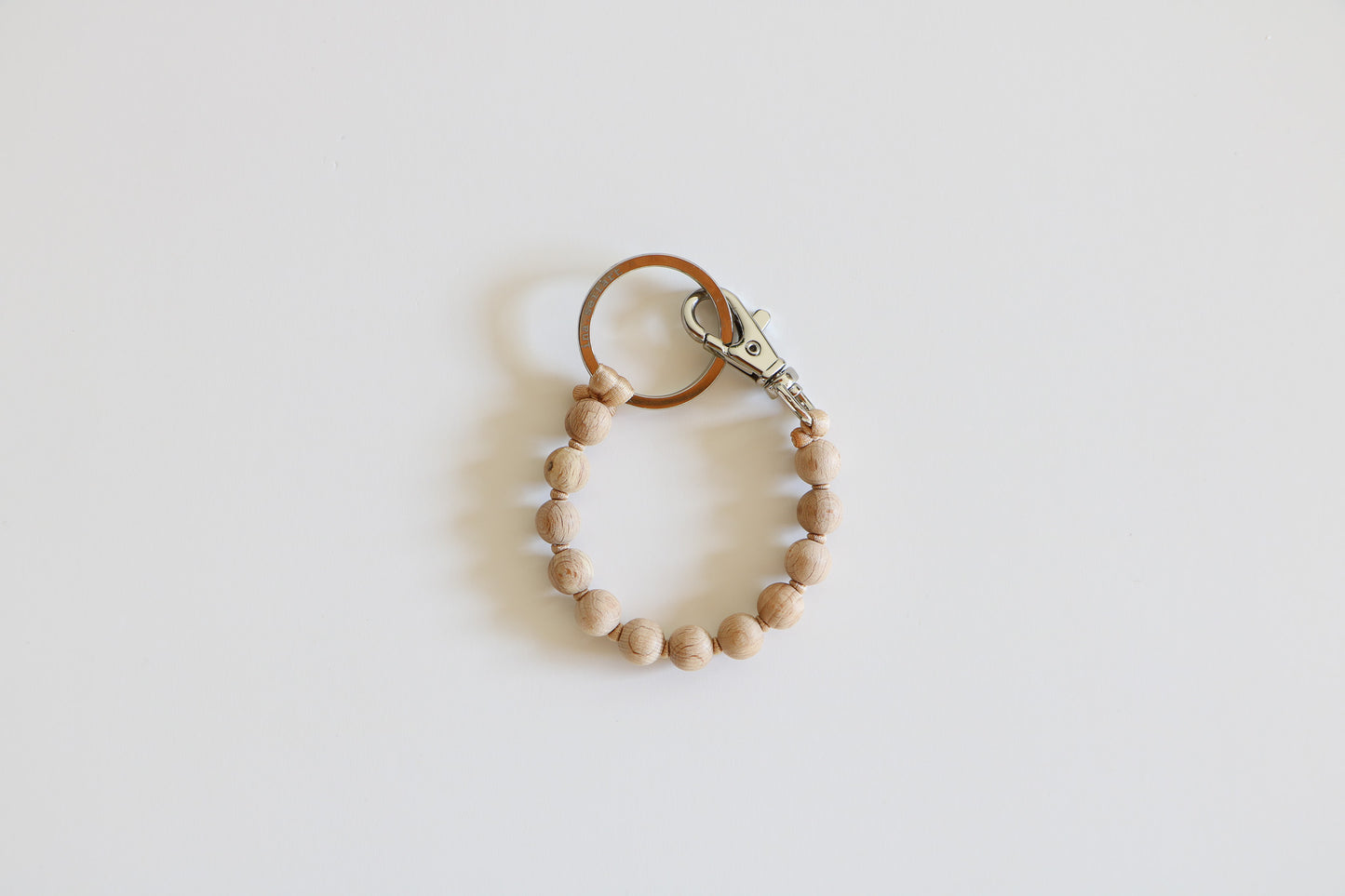 Natural wooden beaded keychain held together with a metal clasp on a light background. 
