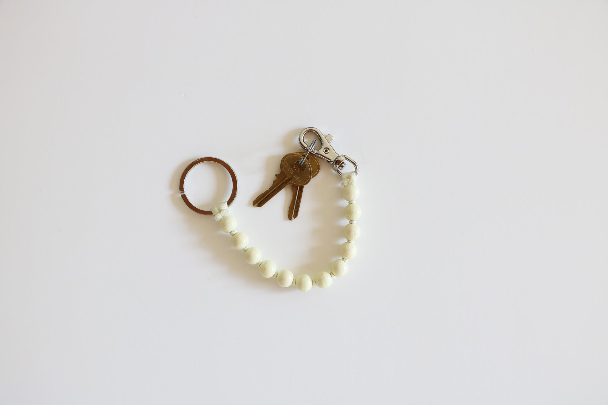 Opal-colored natural wood beaded keychain with a metal clasp, made by Ina Seifart, on a natural white background.