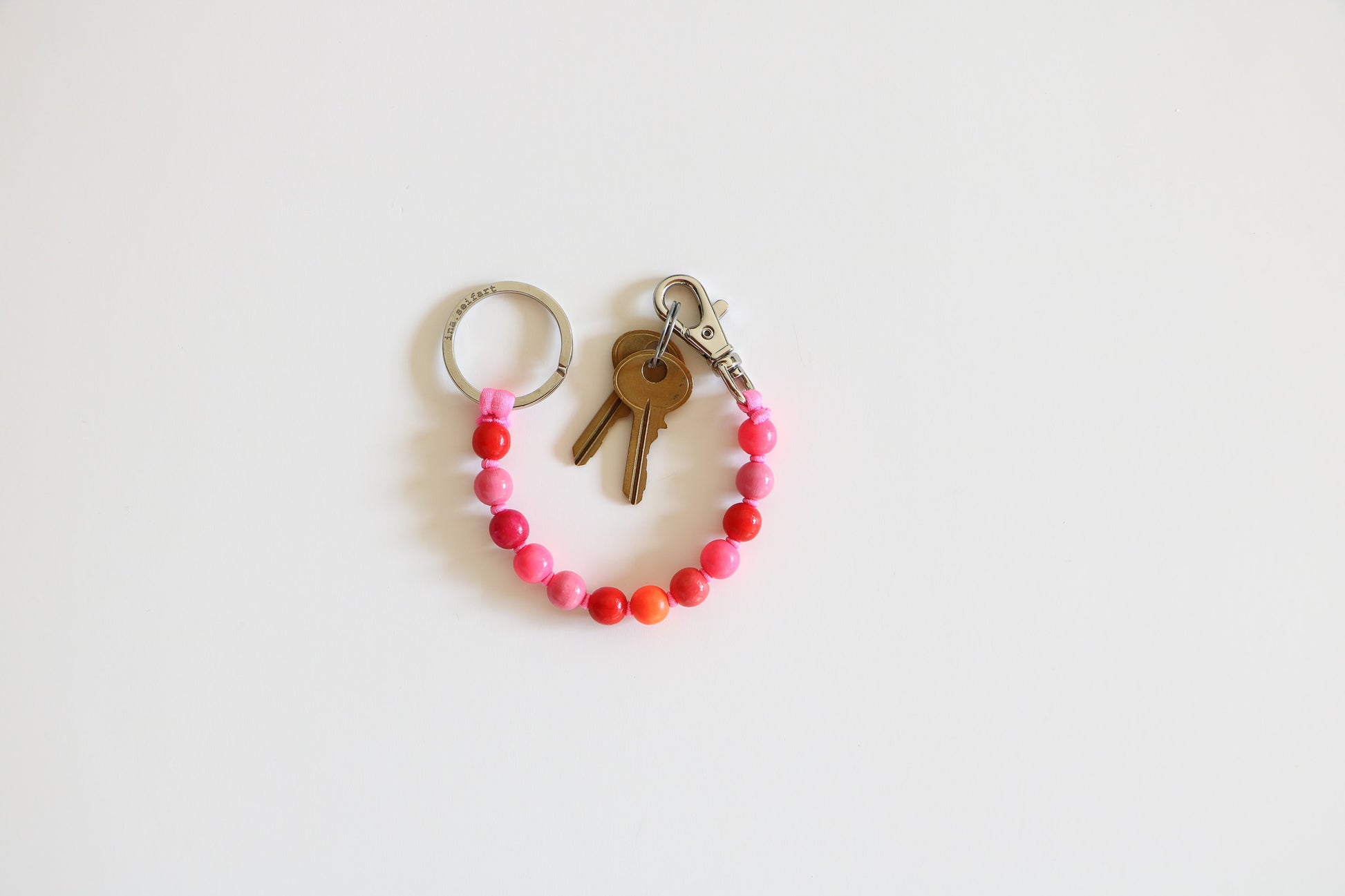 Pink multi-colored natural wood keychain arranged in a semi-circle. Metal ring on one side, metal clasp and two small brass keys on the other. Beads are light and medium pink, red, and orange. 