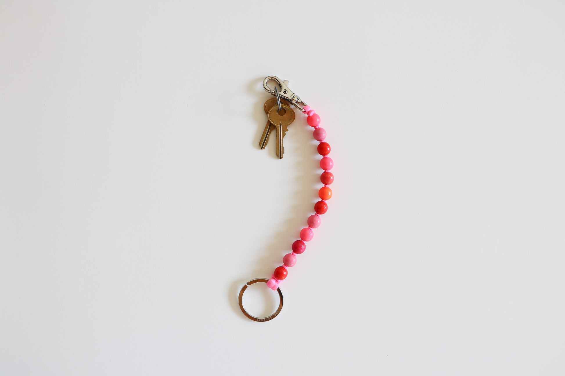 Multi-colored pink wood beaded keychain  with a metal clasp on a light background. Beads are light, and medium pink, red, and orange. 