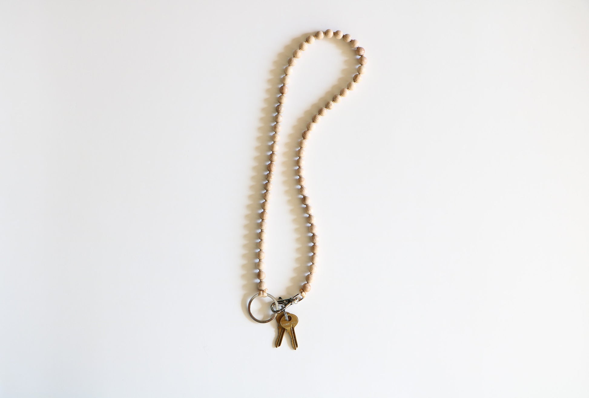 Natural wood Ina Seifart beaded keychain, laying naturally on a white background, attached at the bottom with two keys and a metal clasp.
