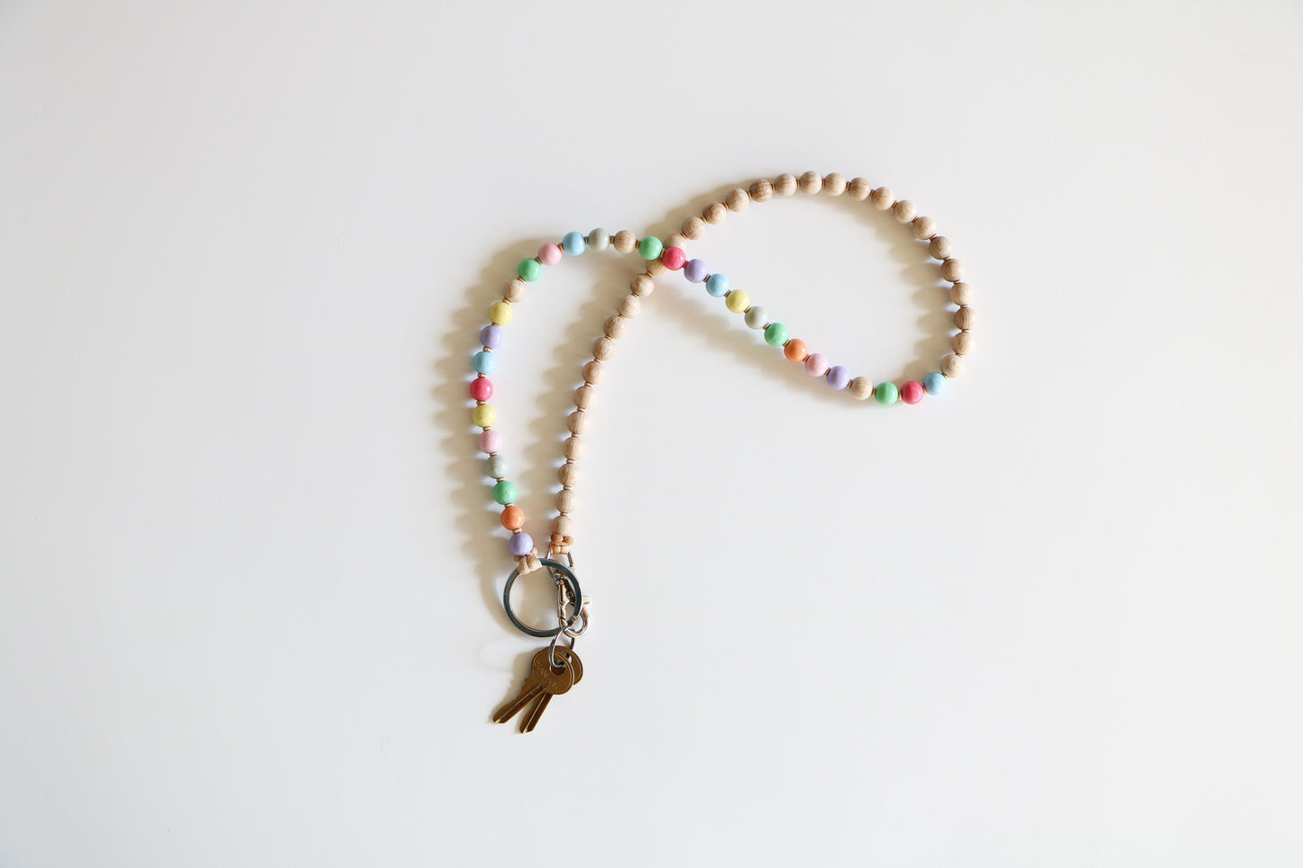 Multicolored wooden bead keychain by Ina Seifart on a white background, with two brass keys connected with a metal clasp. Keychain features half pastel colors, half natural wooden beads.