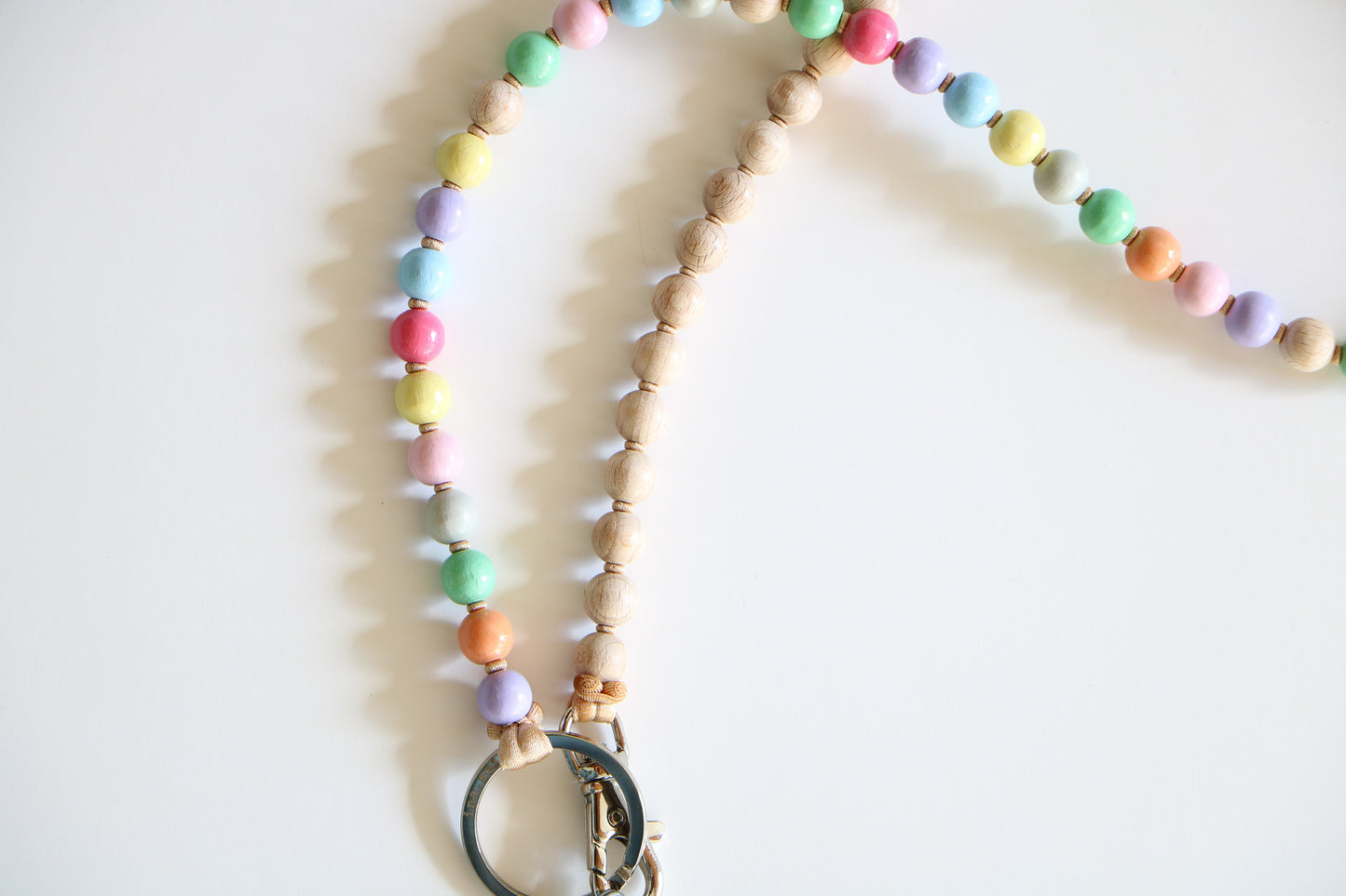 Close up of wooden beads on a threaded keychain, with a metal ring on the bottom. Half pastel rainbow colors, half natural wooden beads.