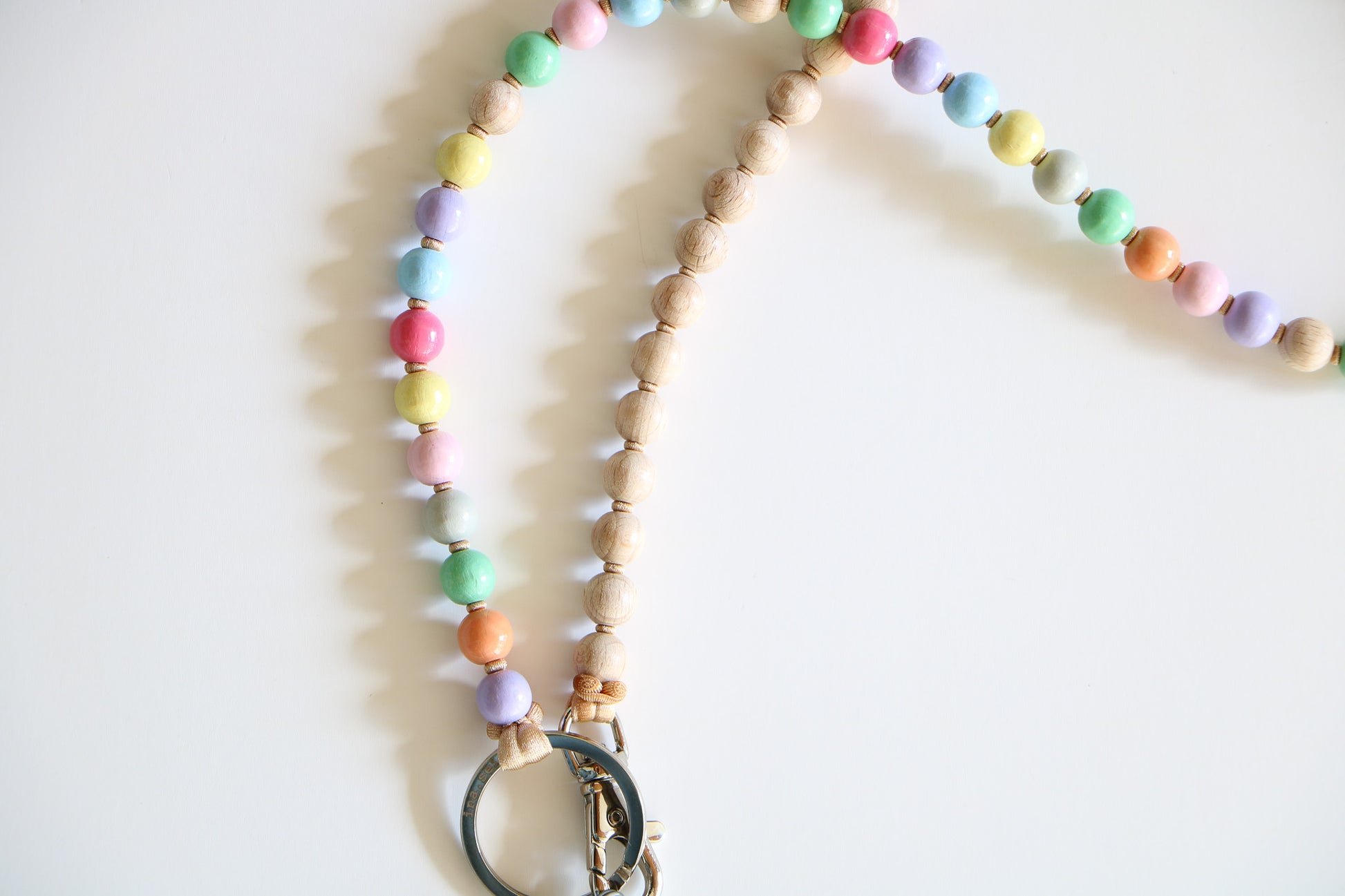Close up of wooden beads on a threaded keychain, with a metal ring on the bottom. Half pastel rainbow colors, half natural wooden beads.
