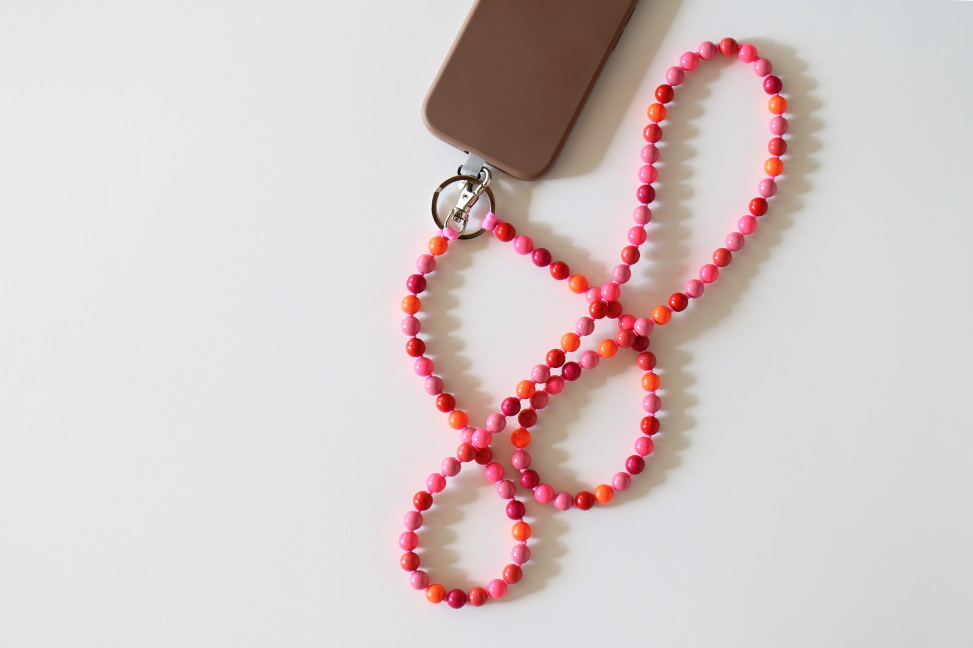 Pink mix threaded wooden bead lanyard connected to phone with a silver clasp. Made by Ina Seifart, the lanyard is a mix of dark pink, light pink, red, and orange beads.