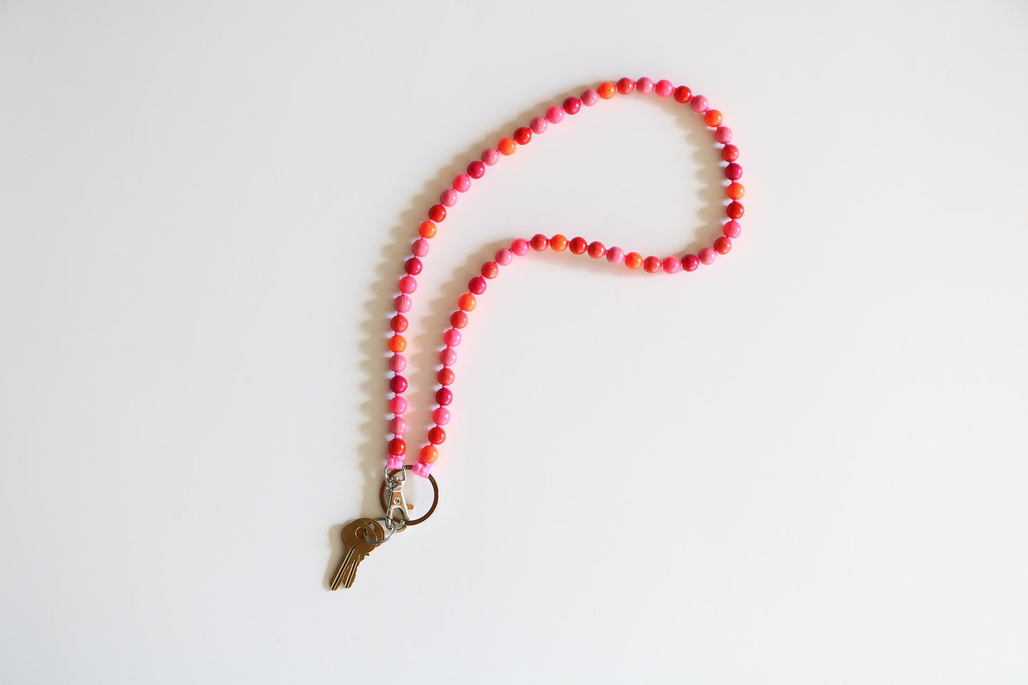 Pink mix wood beaded keychain by Ina Seifart, laying flat naturally with magenta, pink, red, and orange bead pattern on a white background.
