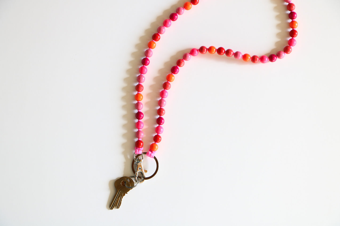 30 inch pink beaded keychain on a white flatlay, connecting to keys with a metal clasp. This keychain is in a 'pink mix' colorway with light pink, dark pink, red, and orange wooden beads.