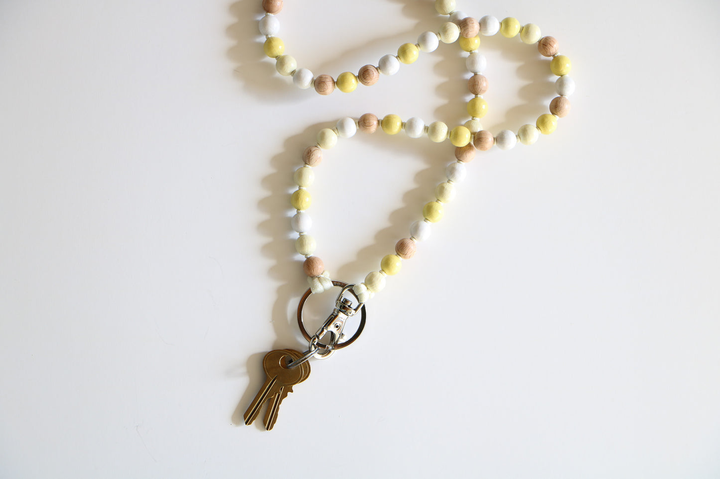Long threaded wooden beaded keychain by Ina Seifart connecting to keys with a metal clasp. Keychain has white, light yellow, and natural wood beads. 