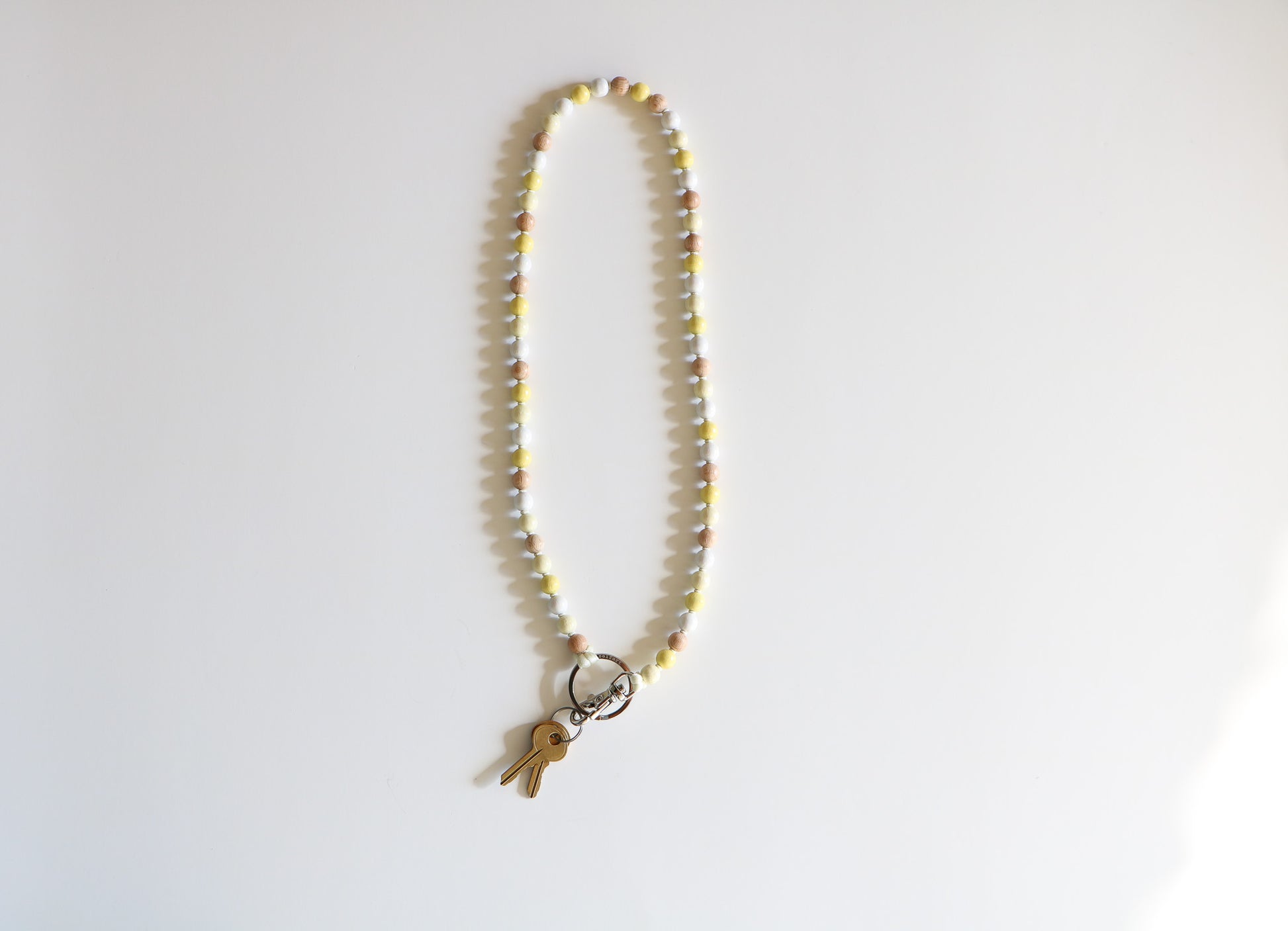 Full Ina Seifart beaded keychain laying flat on a white background. Approximately 30 inches long in an oval shape, with white, yellow, and natural wood beads pattern.