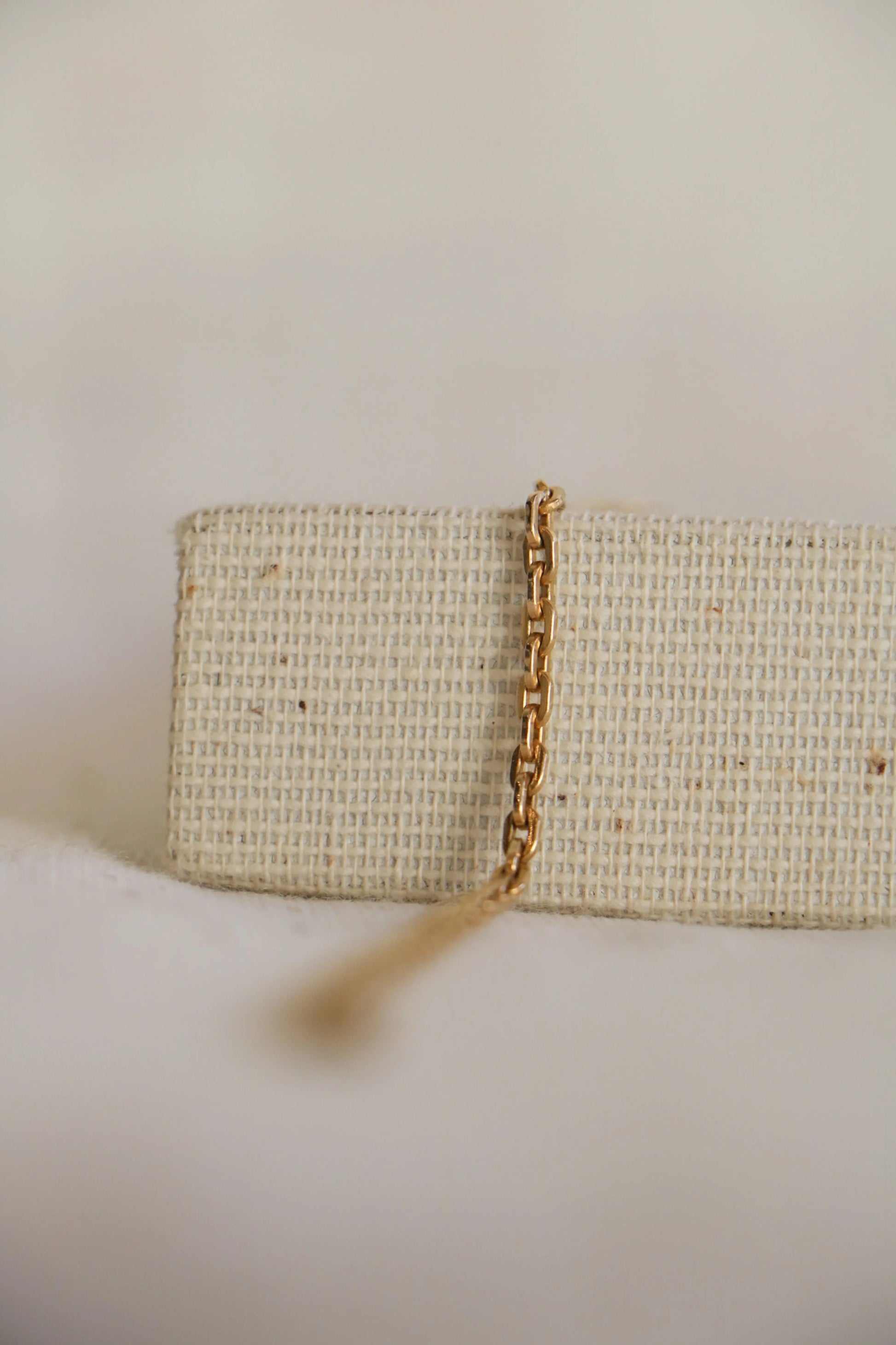 Thick gold-filled 'Cable Link' with oval jewelry links on a chain draped over a woven jewelry holder, on a light background.