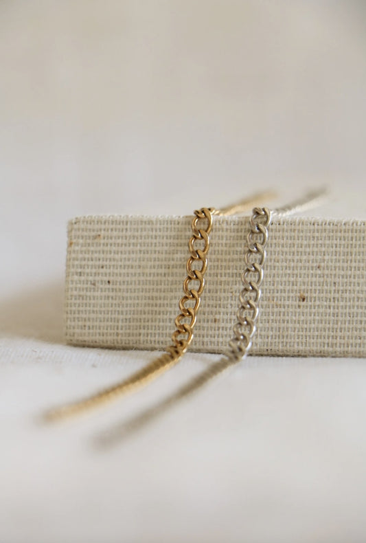 Large 3mm gold-filled and sterling silver permanent bracelets laid across a neutral surface to showcase the chain.