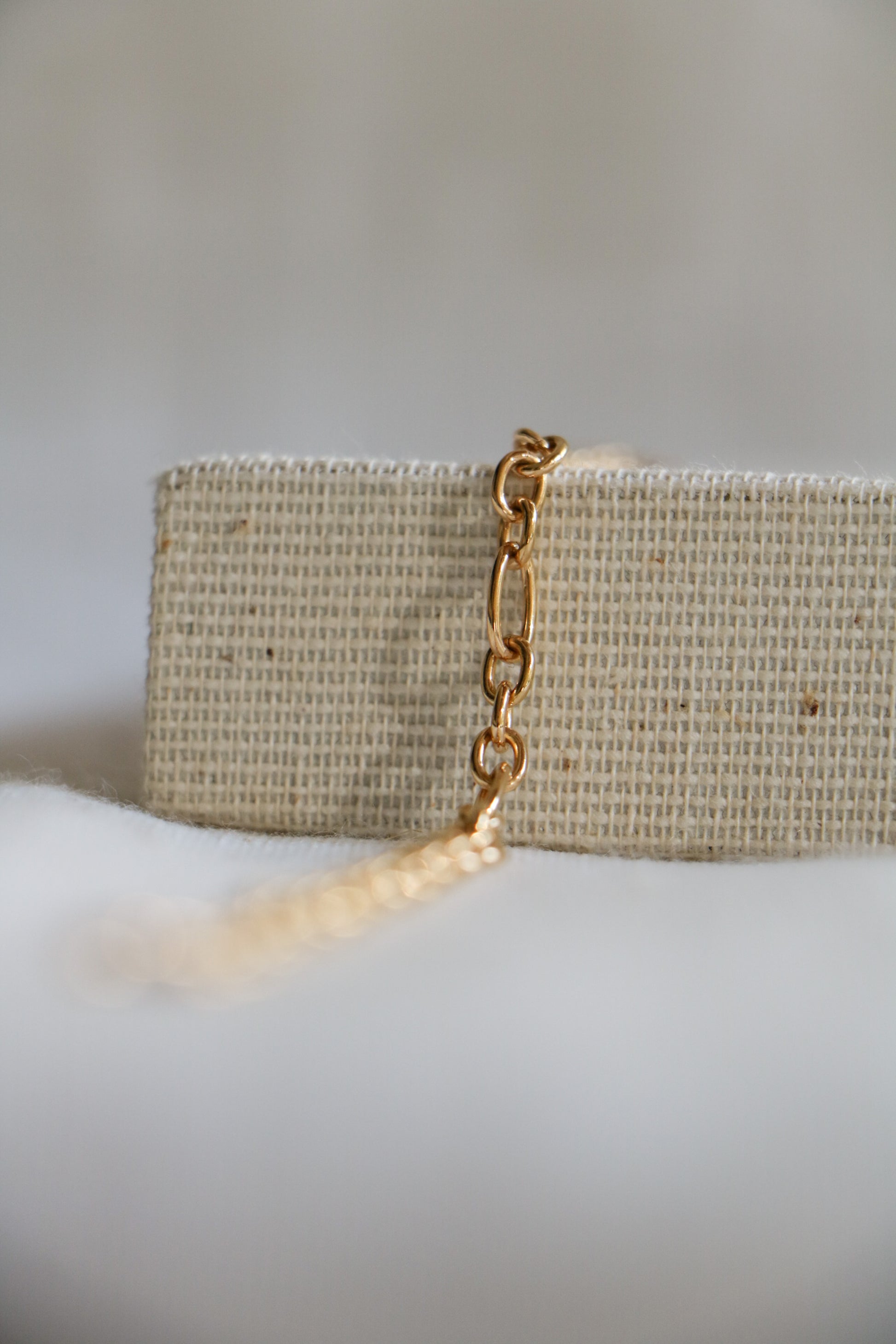 Large permanent jewelry link called the 'Large Oval Link', shown in gold-filled, with 3 large circular links followed by a large oval link in a pattern. Sitting on a woven jewelry holder and white blurred background. 