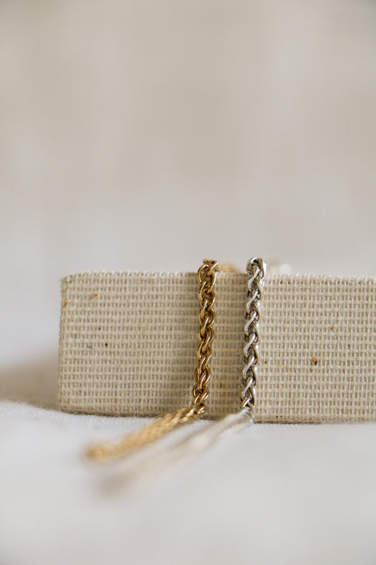 Two permanent jewelry links, our Large Wheat Link, in gold-filled and sterling silver on a woven background.