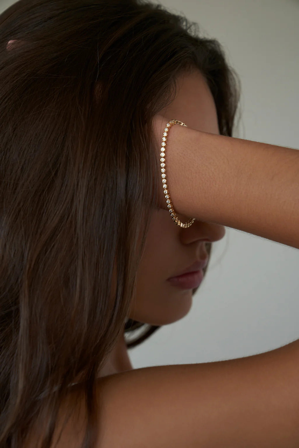 Mini tennis bracelet on a woman's wrist, with gold-plated brass connectors, and 2mm cubic zirconia diamonds around it.